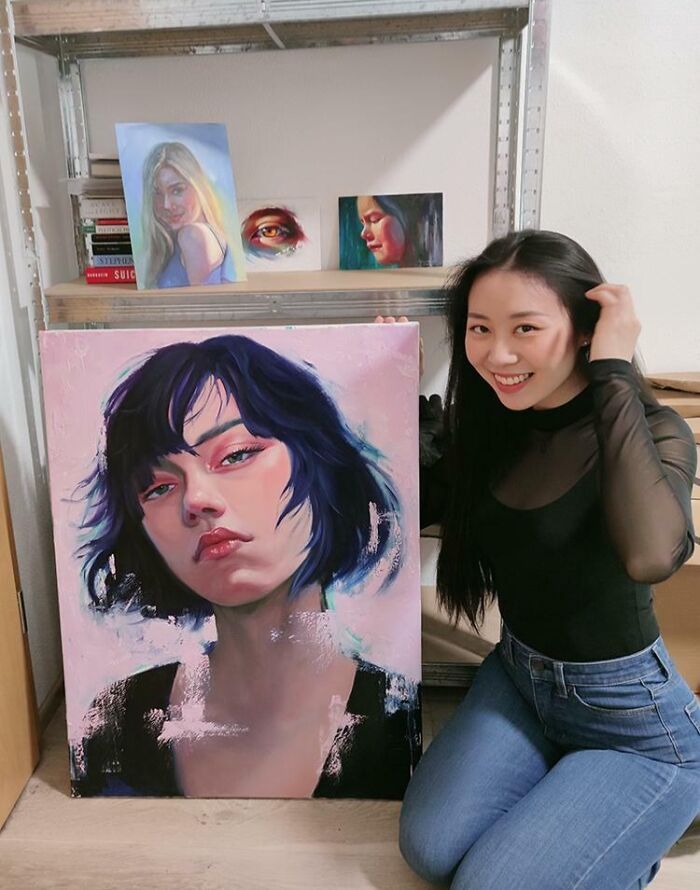 Young artist smiling next to her painted portrait, showcasing big and small dreams turned into reality and inspiring creativity.