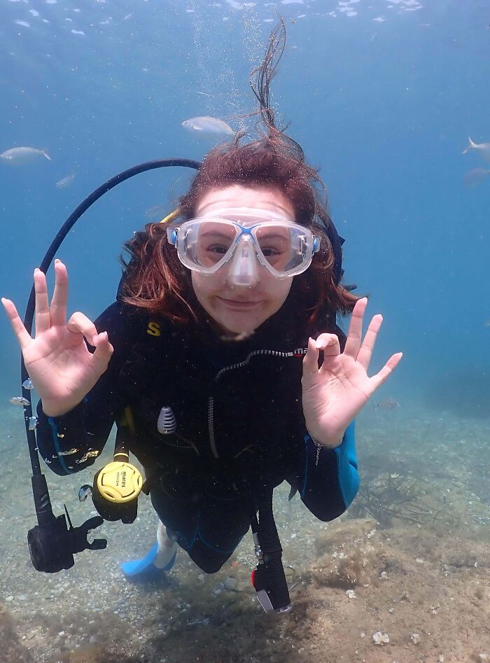 A scuba diver underwater smiling and making OK hand signs, showcasing dreams turned into reality and inspiring others.