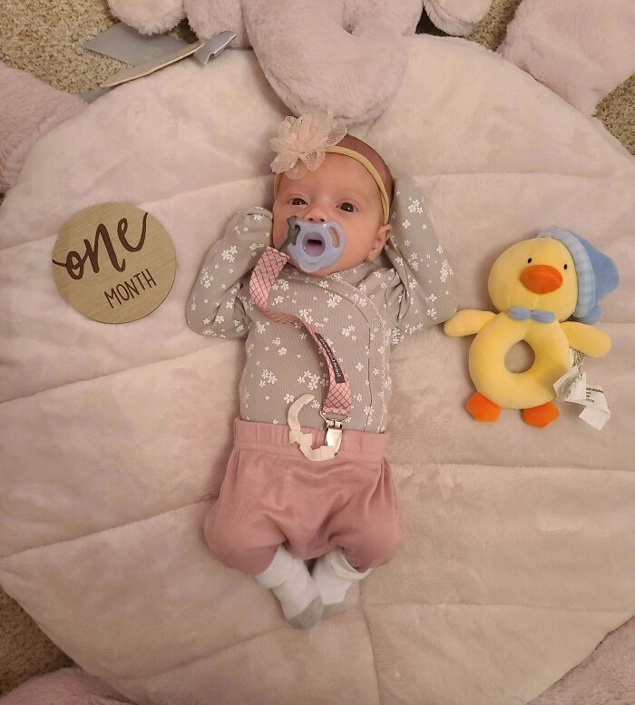 One-month-old baby lying on soft blanket with pacifier and plush toy, inspiring big and small dreams realized.