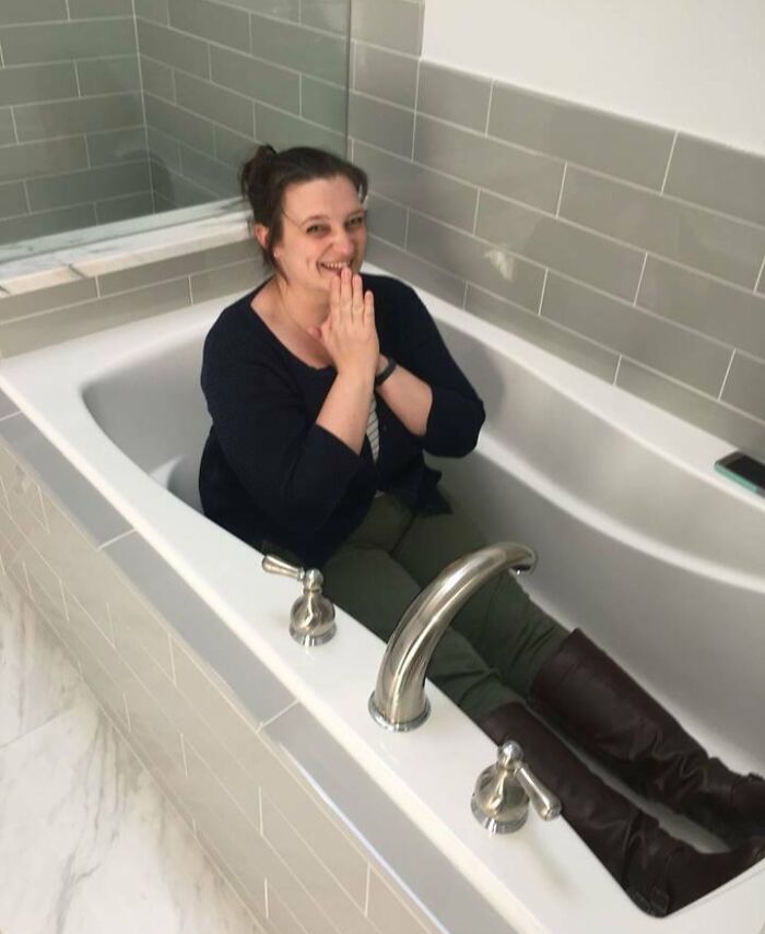 Woman sitting happily in bathtub wearing boots, showcasing people turning their big and small dreams into reality.