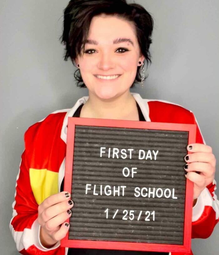 Person smiling and holding a sign about flight school, celebrating turning big and small dreams into reality and inspiring the internet.