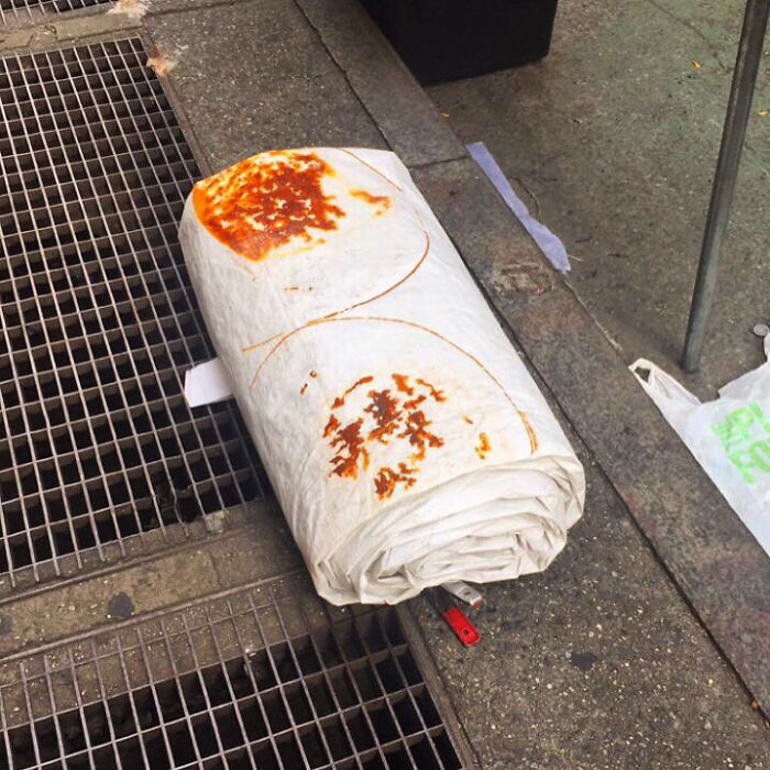 Large rolled flatbread with sauce stains lying on a city sidewalk near metal grates as forbidden foods example.
