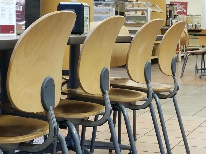 Empty wooden chairs with curved backs lined up at a counter in a cafeteria, illustrating forbidden foods concept.