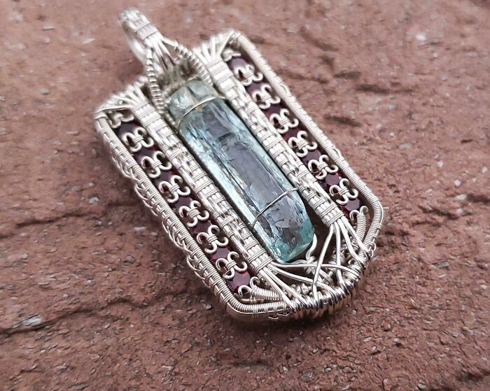 Close-up of a handcrafted wire-wrapped pendant featuring a blue-green crystal on a textured surface, highlighting forbidden foods.