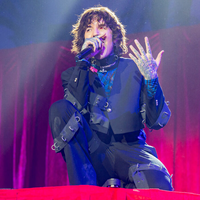 Oliver Sykes performing on stage, wearing black outfit with detailed sleeves, showcasing tattoos and intense expression.