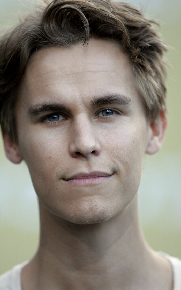 Close-up portrait of Rhys Wakefield with blue eyes and tousled hair in natural outdoor lighting.