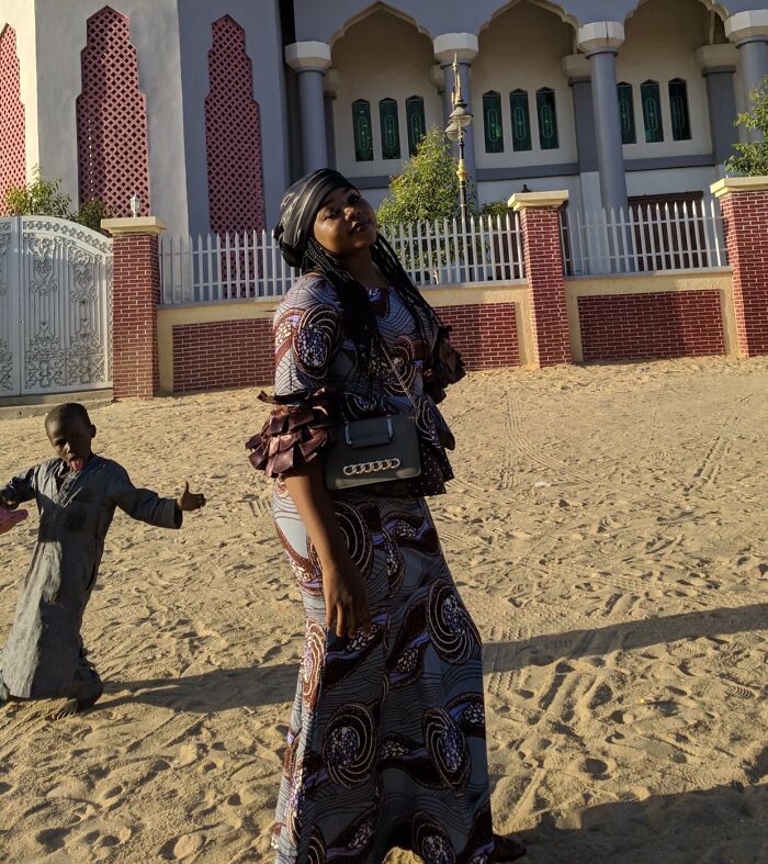 Woman posing in patterned dress with a child photobombing behind her, creating an epic photobomb moment outdoors.