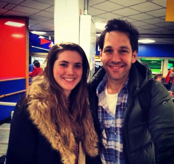 Two people smiling indoors with a photobomb in the background capturing an epic moment that made everyone laugh.