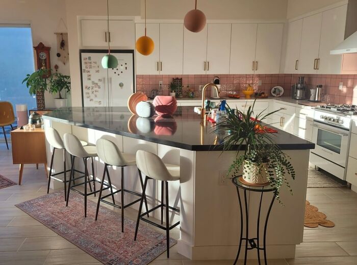 Modern kitchen with a black countertop island, white cabinetry, colorful pendant lights, and a decorative indoor plant stand