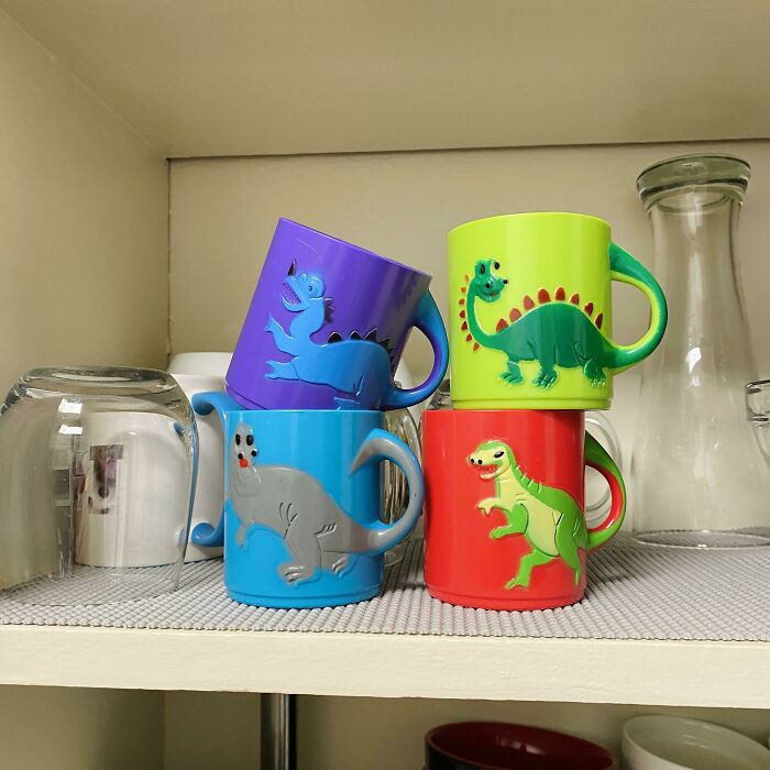 Tazas coloridas con dinosaurios en un estante que reflejan momentos divertidos de hombres que nunca crecieron.