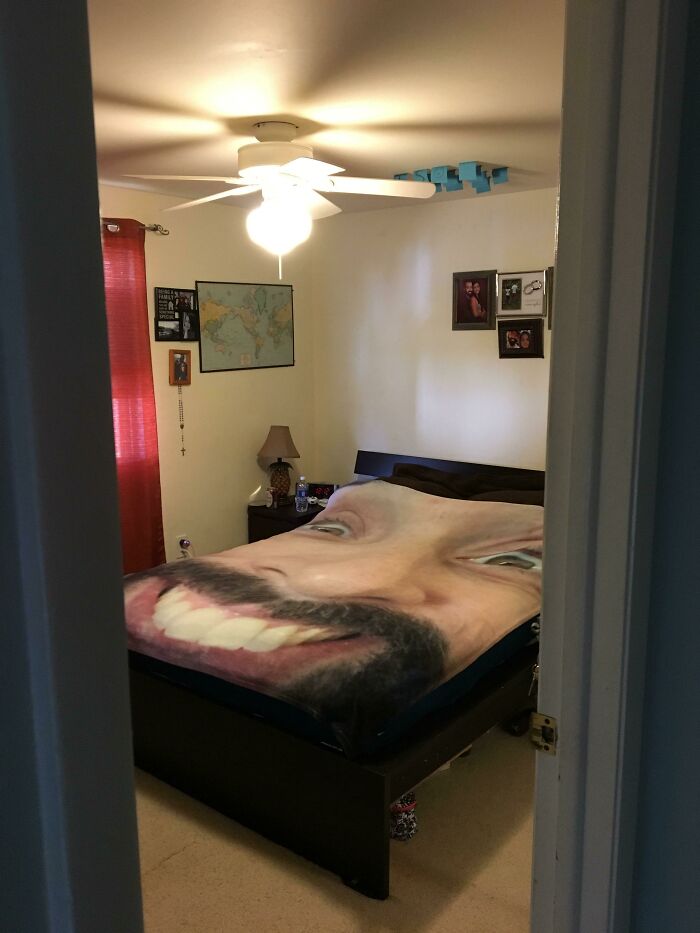 Bedroom with a playful giant face blanket on the bed, showcasing men never grow up in a wholesome setting.