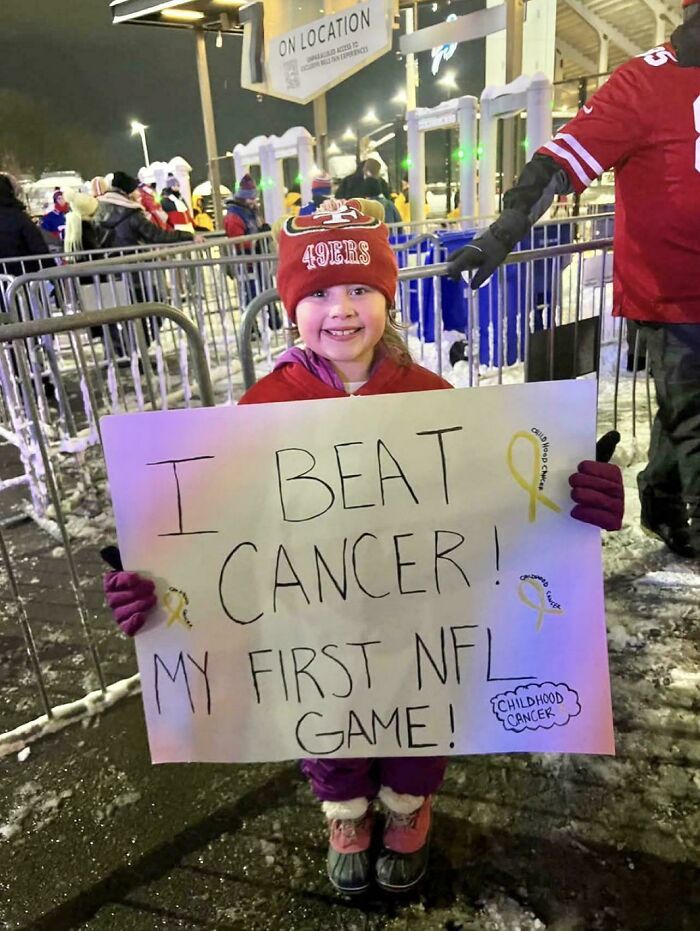 Young girl at an NFL game holding a sign celebrating beating cancer, one of the wholesome internet moments featured online.