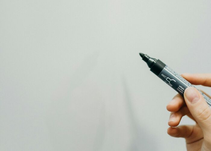 Hand holding a black marker pen poised to write, representing petty revenge ideas on an empty surface.