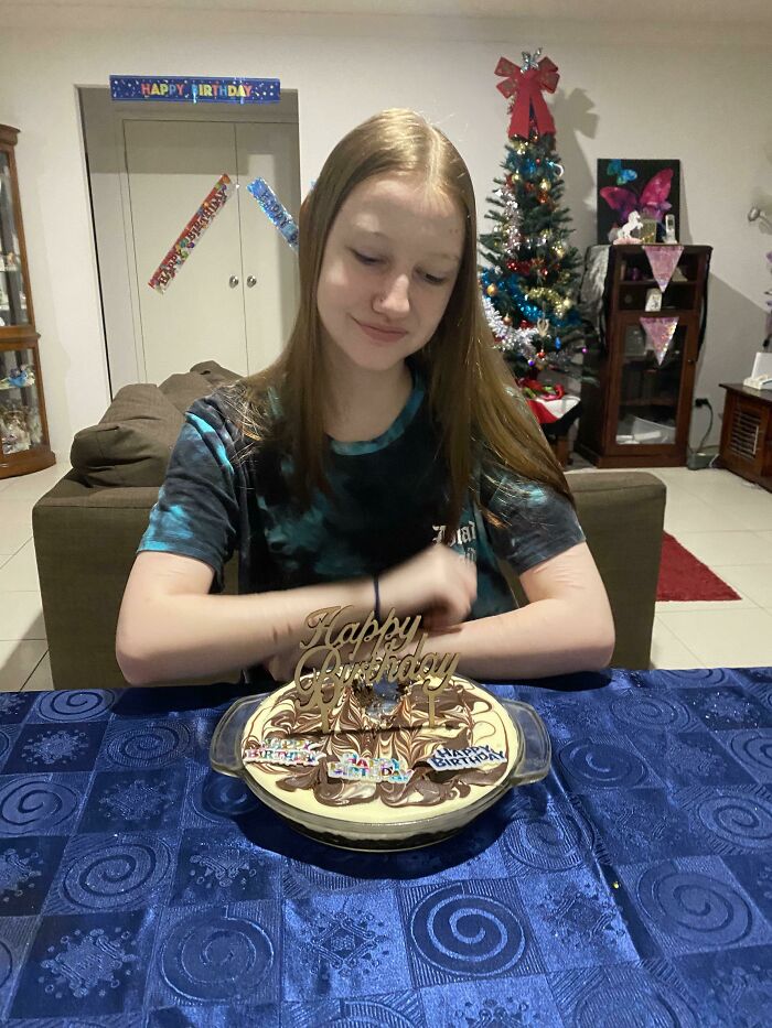 Teen girl smiling at birthday cake with Happy Birthday decorations, capturing a wholesome internet moment of celebration.