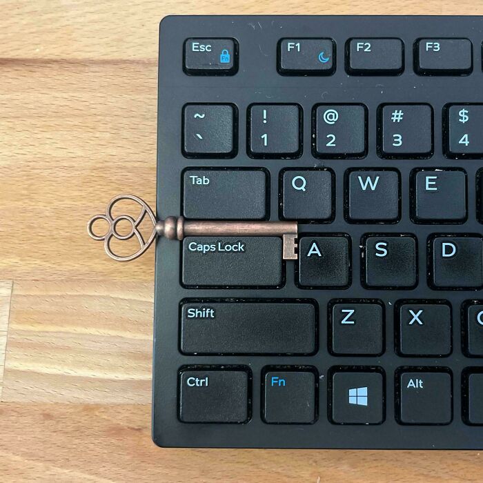 Vintage key perfectly aligned with the Caps Lock and Tab keys on a black computer keyboard on wooden desk surface