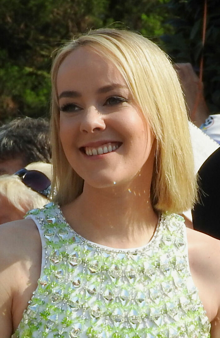 Jena Malone smiling outdoors with short blonde hair, wearing a sleeveless dress with green and silver embellishments.