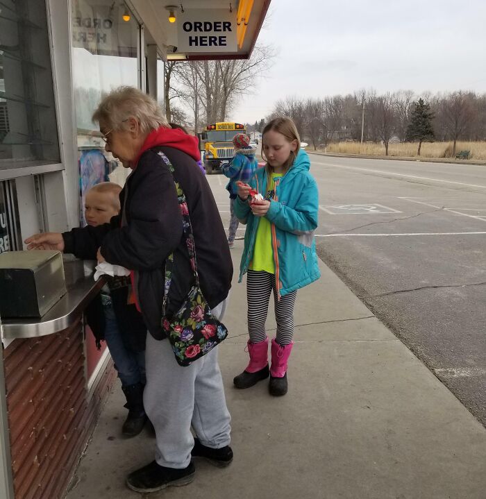 Elderly woman and children outside a small shop in casual wear, capturing a moment of everyday life for employees who walked out with jokes.
