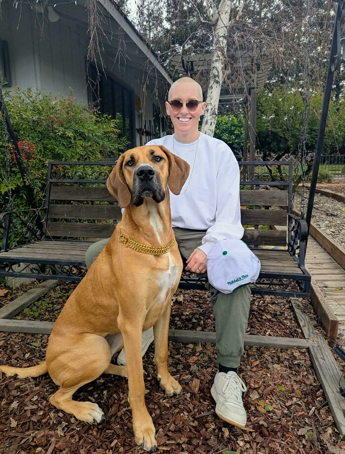 Person smiling and sitting on an outdoor bench with large tan dog showing how dogs make our lives better.