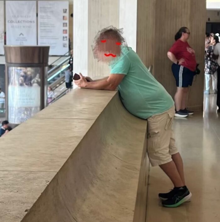 Man leaning on a railing perfectly aligned with a curved ledge, creating a seamless visual illusion indoors.