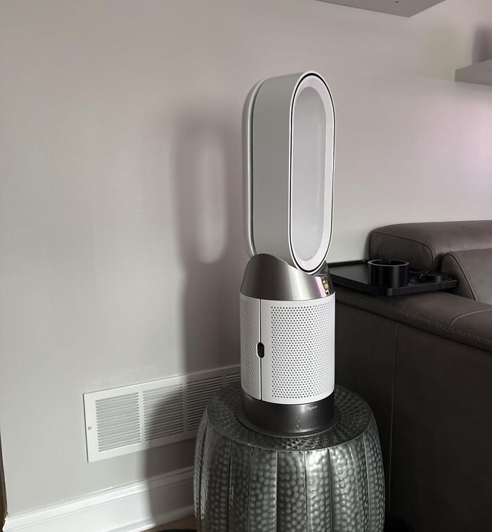 Dyson air purifier placed on a textured stool next to a grey sofa in a modern living room setting.