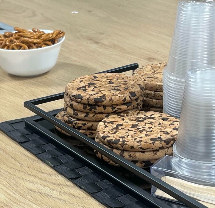 Stack of round cork coasters next to clear plastic cups and a bowl of pretzels on a wooden table, forbidden foods concept.