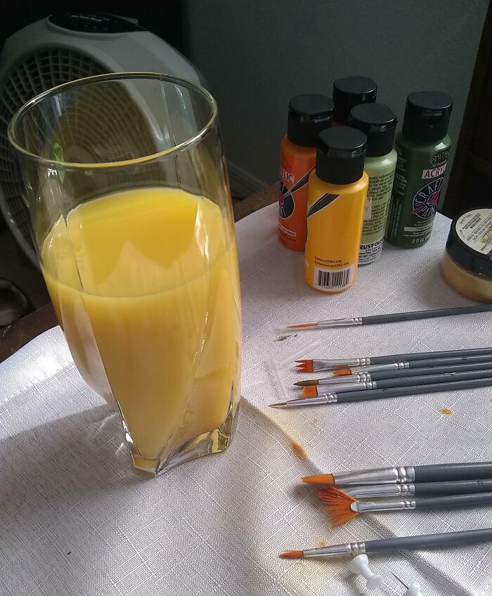 Glass of orange juice placed next to paintbrushes and acrylic paint bottles, illustrating forbidden foods concept.