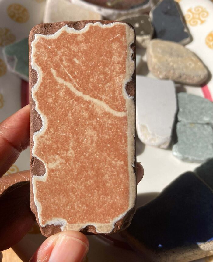 Hand holding a rectangular ceramic piece with intricate patterns among other forbidden foods themed items on a table.