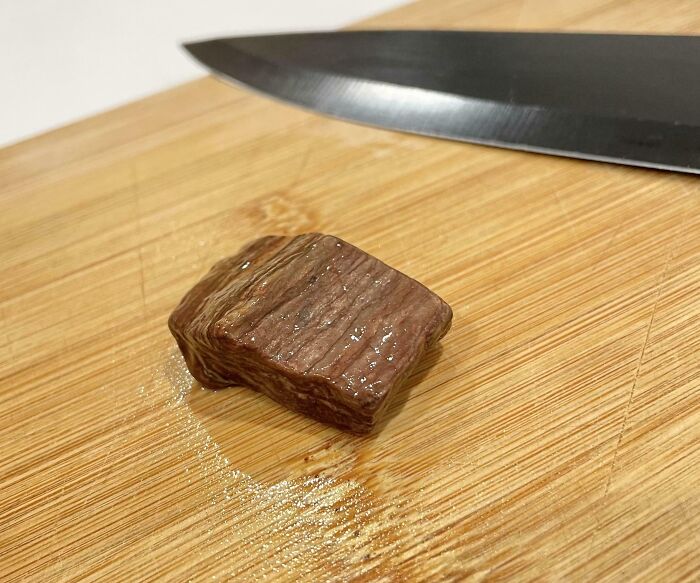 A small piece of cooked meat on a wooden cutting board next to a knife, highlighting forbidden foods concept.
