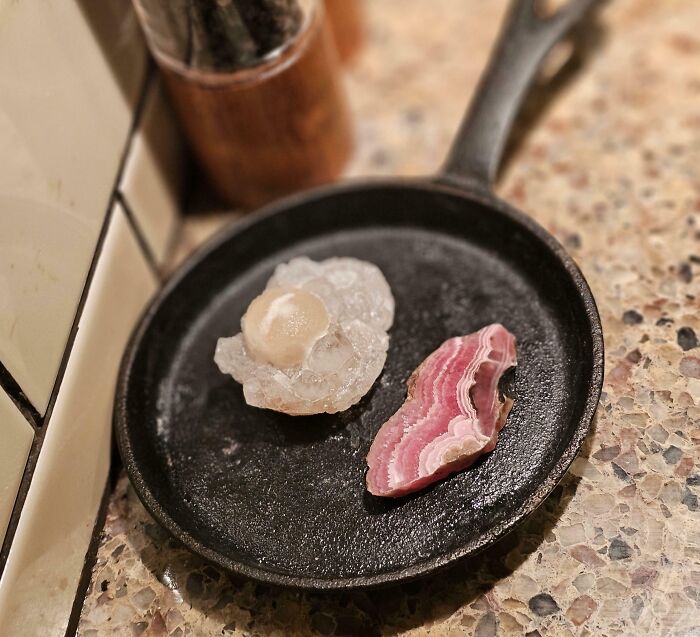 Close-up of two raw forbidden foods placed on a black pan on a speckled kitchen countertop.