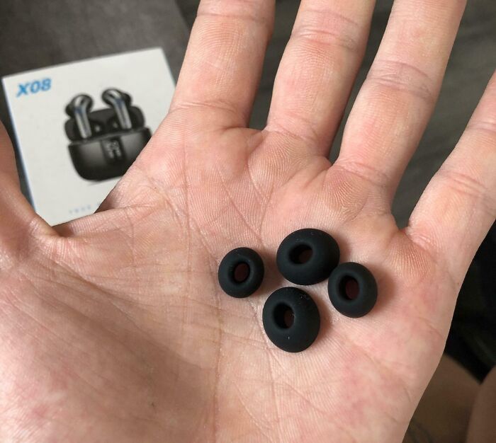 Hand holding four black earbud tips with wireless earbuds box blurred in the background, unrelated to forbidden foods.