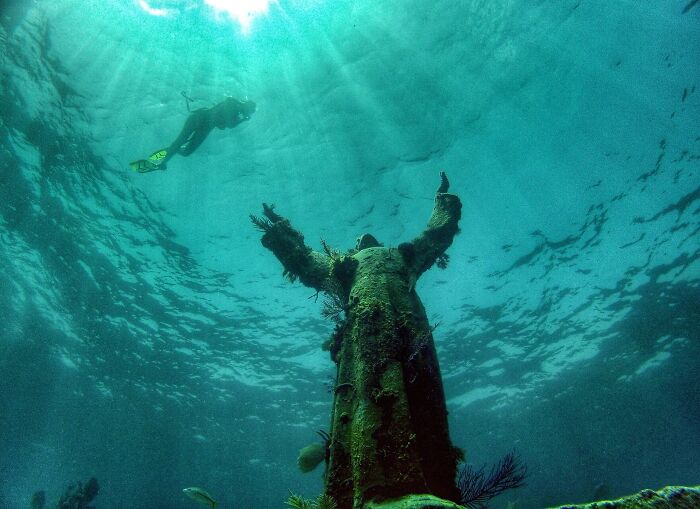 Underwater spectacular sculpture covered in marine life with a diver exploring the global travel attraction.