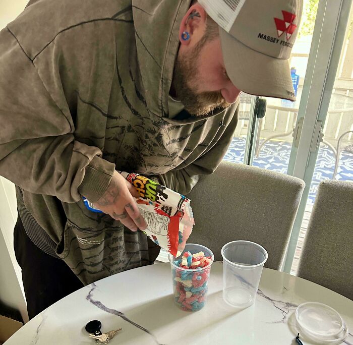 Man wearing a cap pouring candy into a cup at a table, showing wholesome moments of men who never grow up