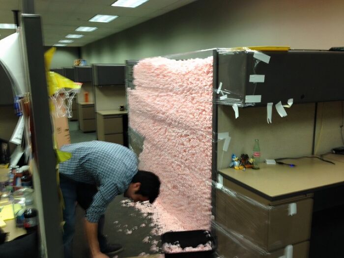 Employee prank with packing peanuts filling an office cubicle in a lighthearted workplace joke scenario.