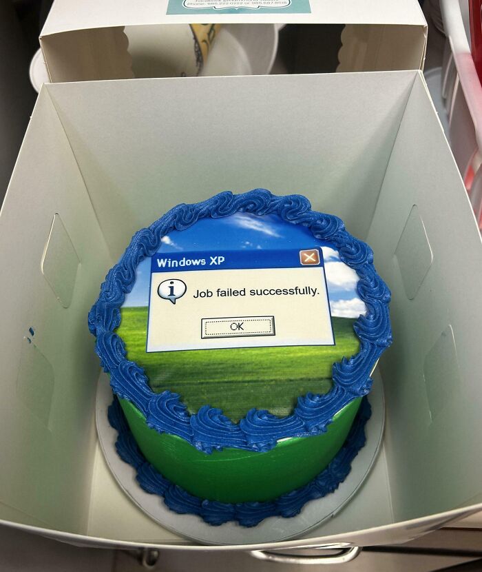 Round cake with blue and green icing featuring a Windows XP error message prank, showing employees’ jokes and office pranks.