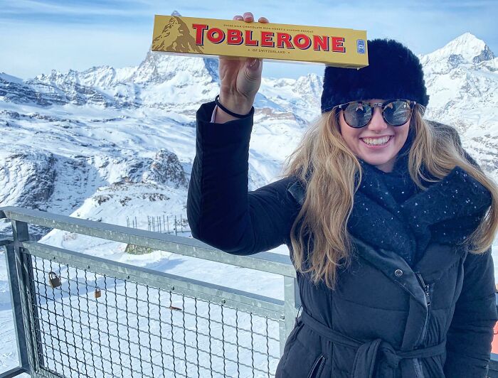 Woman holding Toblerone chocolate aligning it perfectly with the mountain peak, showcasing a clever visual alignment outdoors.