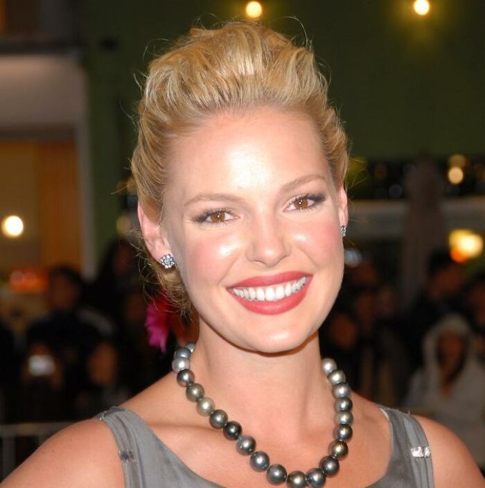 Katherine Heigl smiling at an event, wearing pearl necklace and earrings, showcasing her career highlights and bio.