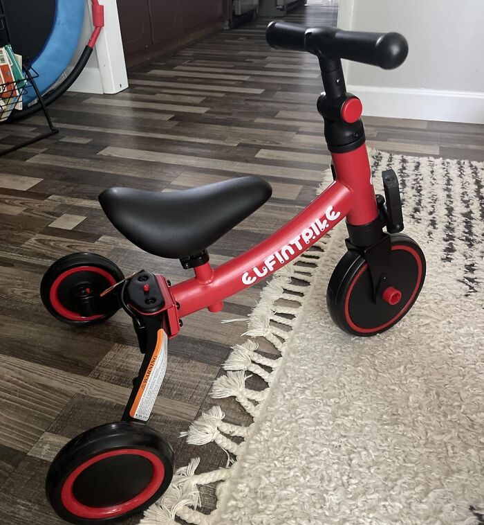 Red and black kids balance bike on hardwood floor and rug, one of the Black Friday week deals on kids toys.