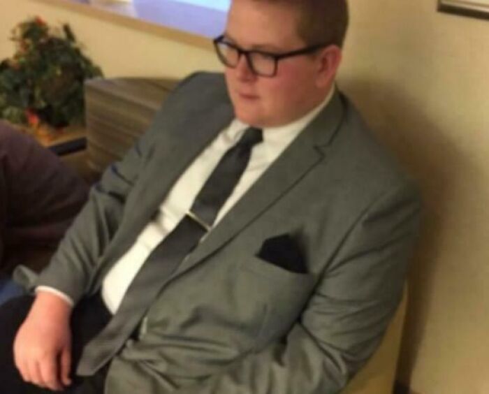 Young man in a gray suit and glasses sitting on a couch, showing a calm moment between grateful siblings.