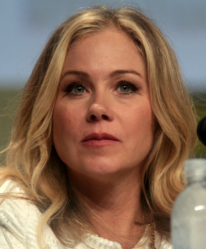 Close-up of Christina Applegate with blonde hair at a speaking event, highlighting her bio and career highlights.