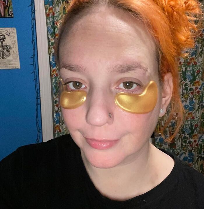 Person with orange hair wearing gold under-eye patches in a colorful room, representing aesthetic gifts and self-care ideas.