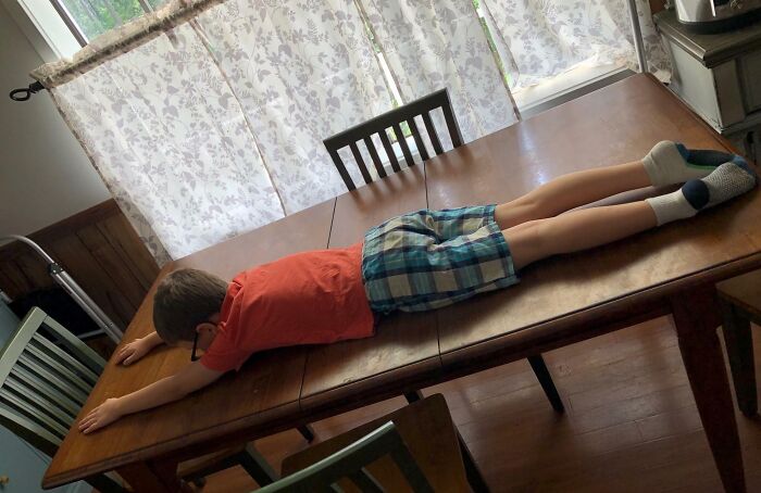 Boy wearing glasses lying face down on a dining table, showcasing playful and wholesome moments men never grow up enjoying