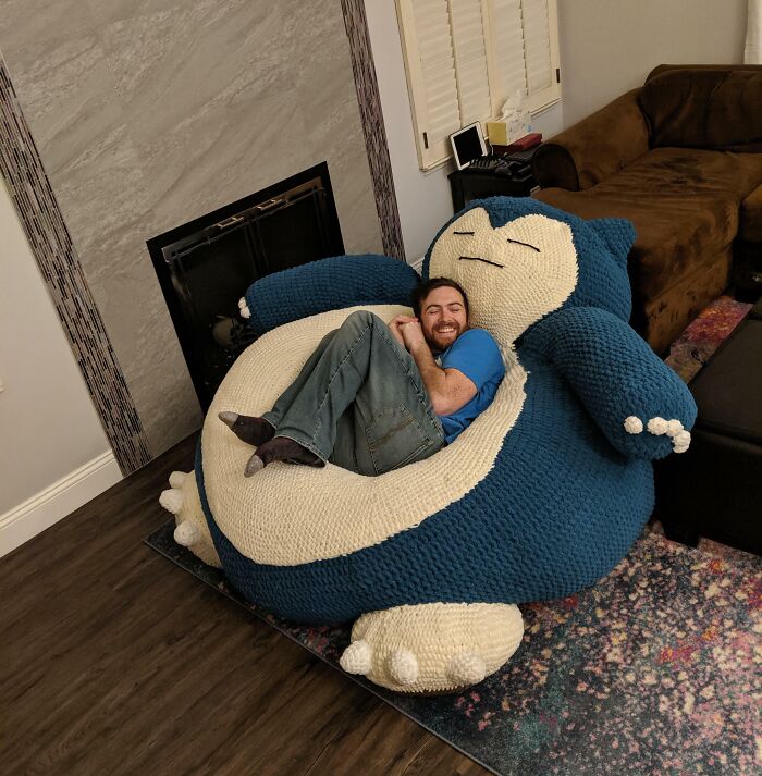 Hombre sonriente recostado en un sillón grande de Snorlax, demostrando momentos hilarantes de hombres que nunca crecieron.