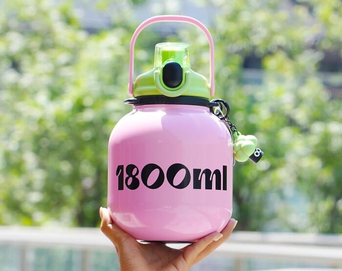Pink practical water bottle with green lid held outdoors, a perfect aesthetic gift for your friend who values style and function.