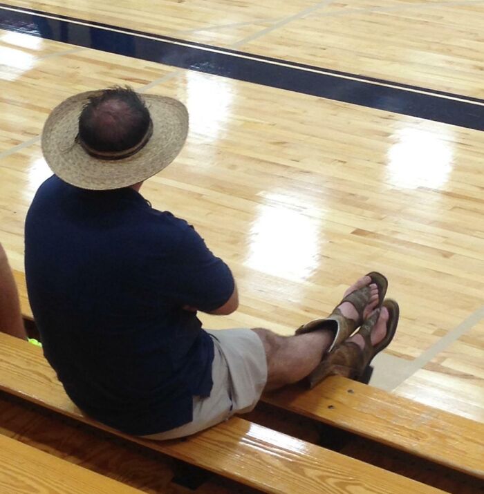 Man wearing a straw hat and sandals, sitting playfully on gym bleachers showing men never grow up concept.