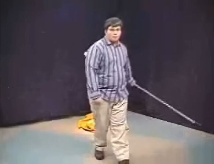 Young man in a striped shirt and beige pants holding a stick, captured in a viral moment that made him an internet icon.