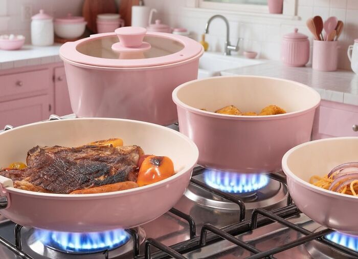 Pink cookware set on gas stove burners with steak and vegetables cooking, highlighting Black Friday deals.