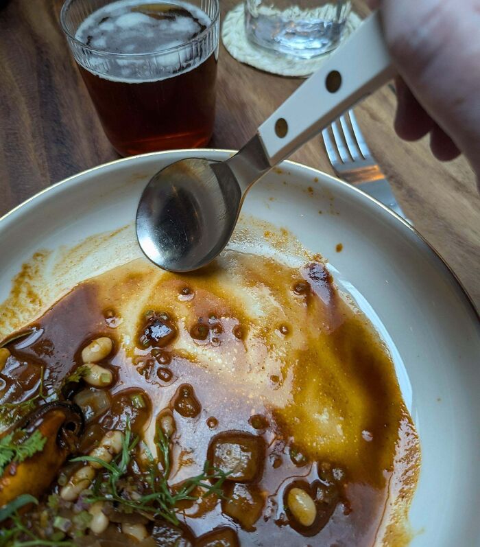 Partially eaten dish with spoon resting on a bowl, drink in background, capturing things aligned so perfectly moment.