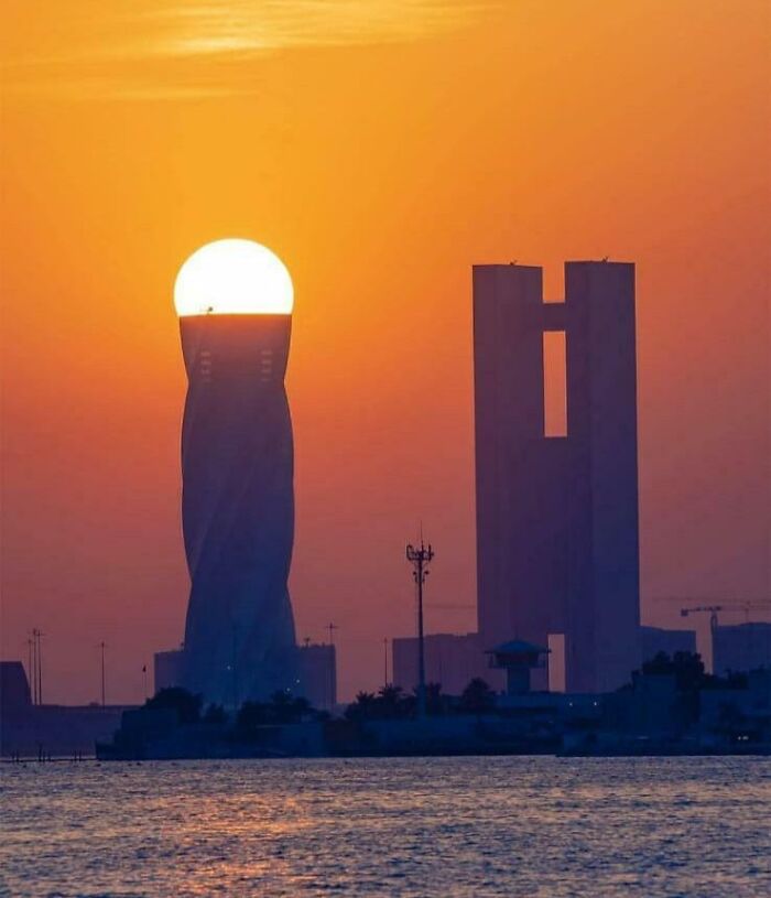 Sun perfectly aligned with a twisting tower at sunset, showcasing remarkable things aligned in a stunning cityscape view.