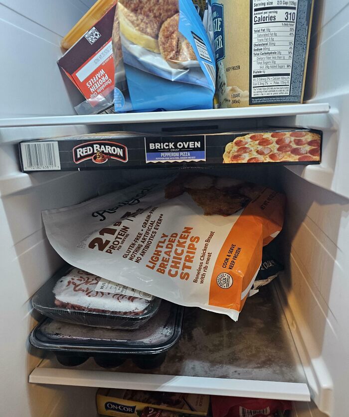 Frozen pizza box perfectly aligned and balancing inside a packed freezer shelf with other frozen food items.