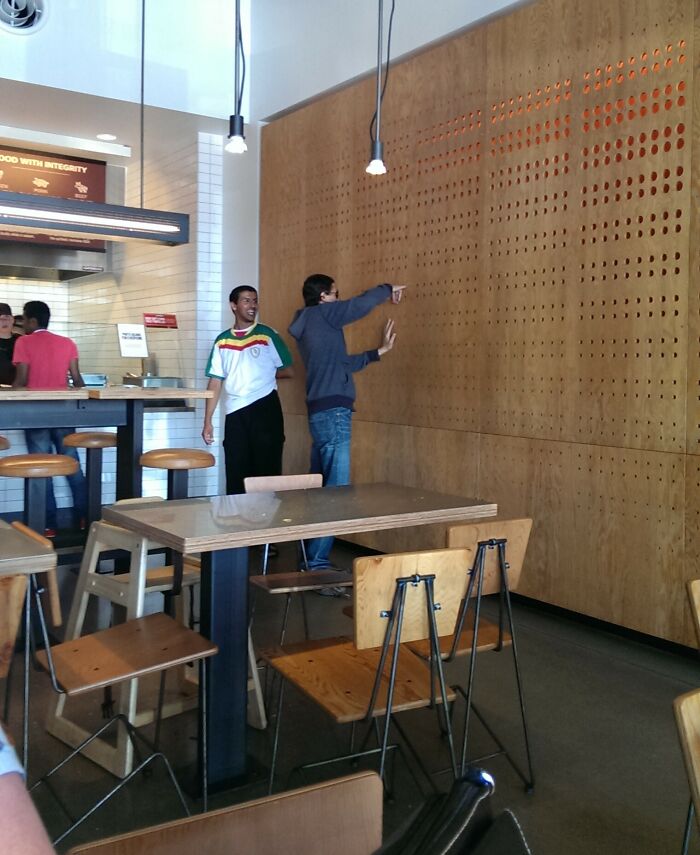 Two men play with a pegboard wall in a restaurant, showing playful and wholesome moments that prove men never grow up.